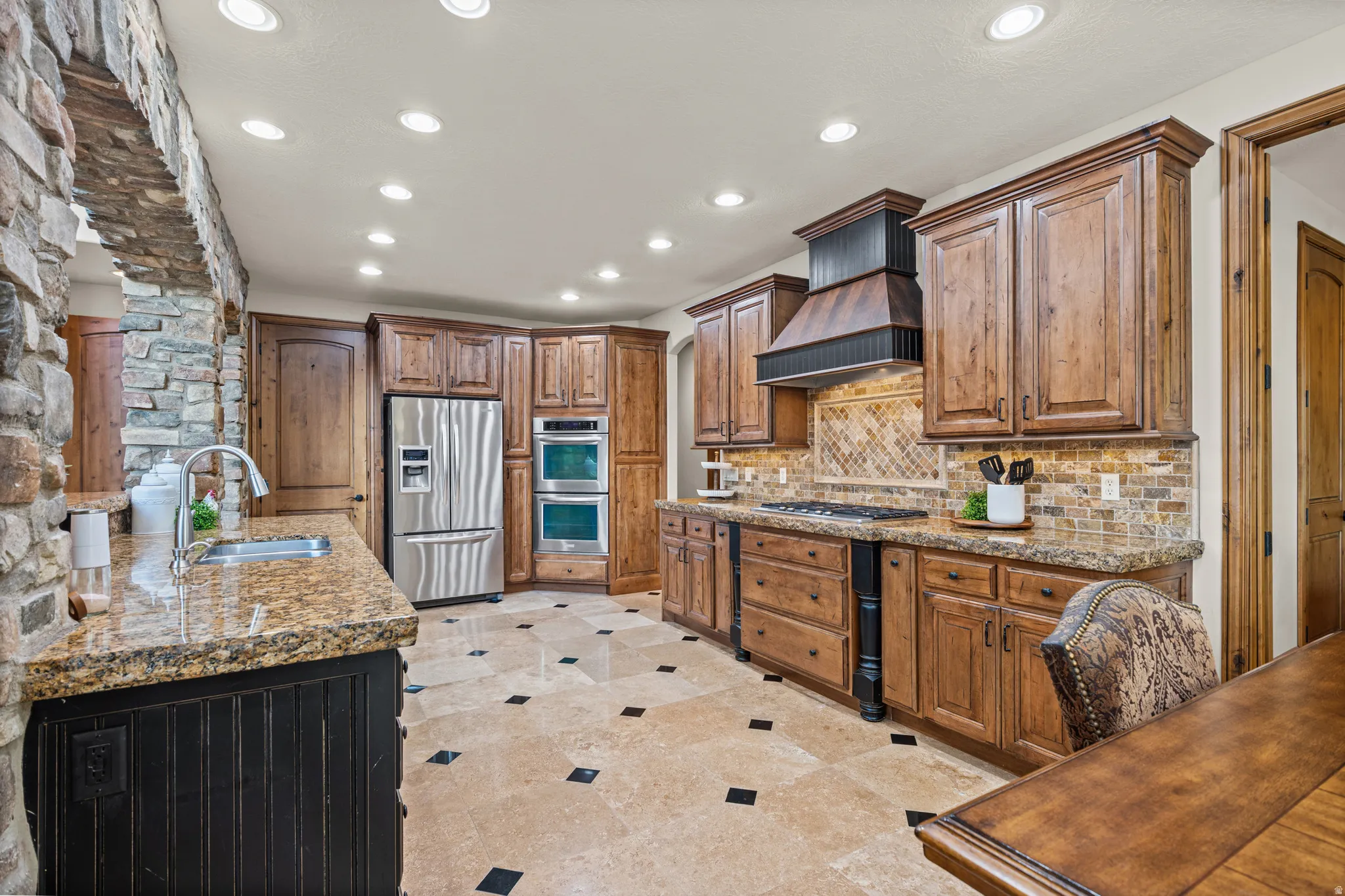 Kitchen featuring rich wood cabinetry, stainless steel appliances, granite countertops, a stone backsplash, and a tiled floor with contrasting accents