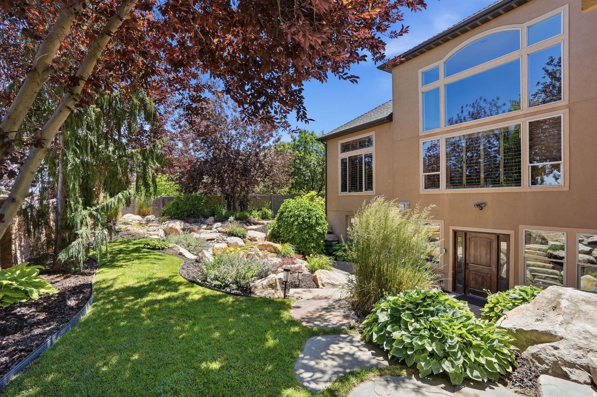 Expansive backyard featuring a manicured lawn, established landscaping, and mature trees