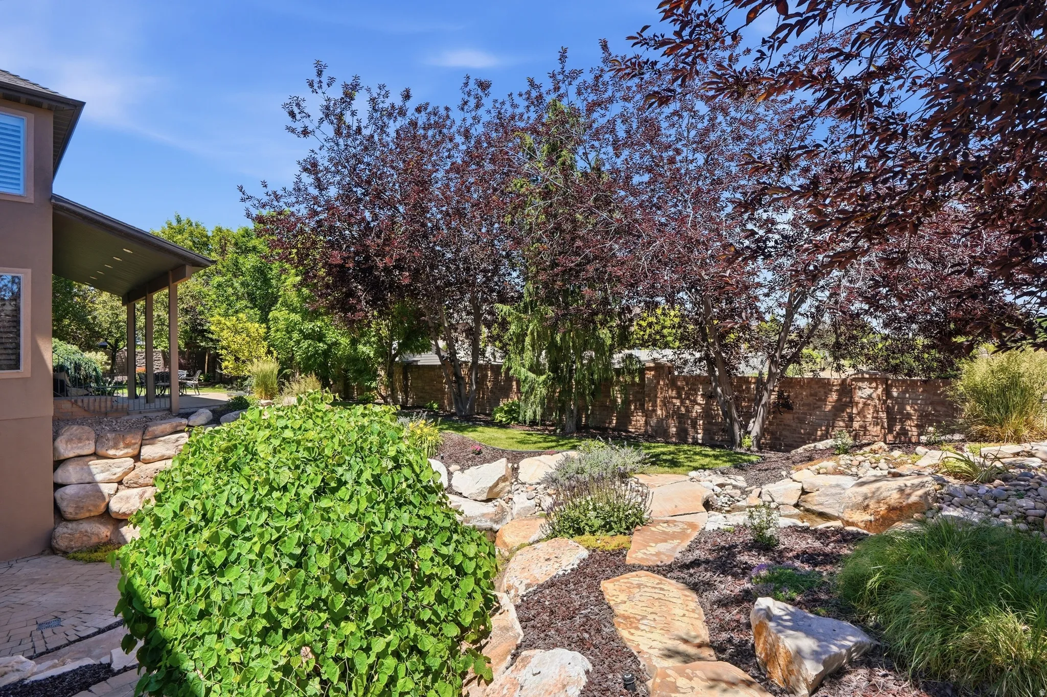 Outdoor living area featuring a covered patio, flagstone-style pathway, and tiered landscaping with natural stone retaining walls