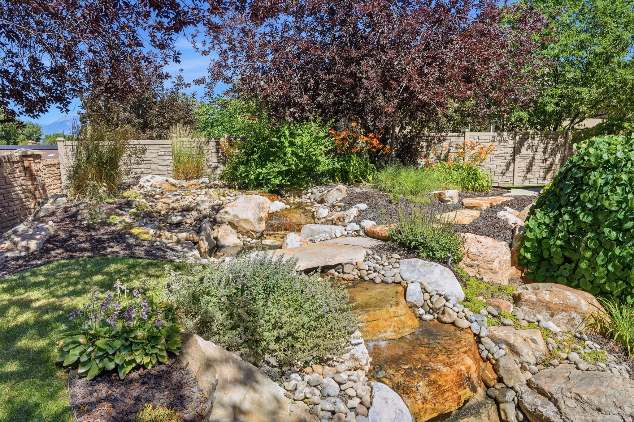 Waterfall with rock formations and varied plantings, featuring a stone wall, mature trees, and ground cover