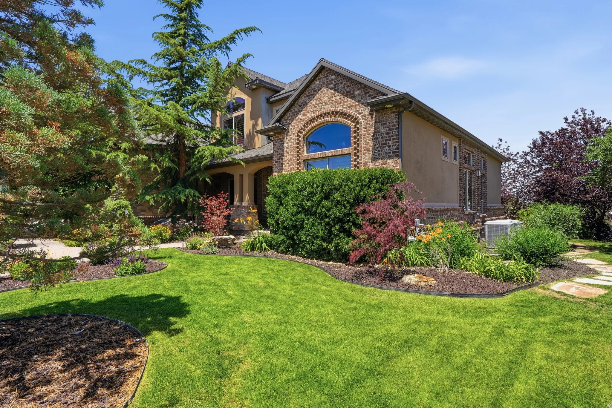 Two-story residence featuring brick and stucco siding with an arched window, a covered entry, and established landscaping