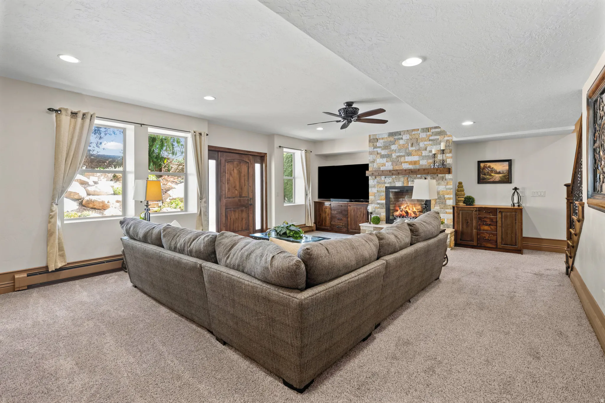 Spacious living area featuring a stacked stone fireplace with a substantial wood mantel, recessed lighting, and a ceiling fan