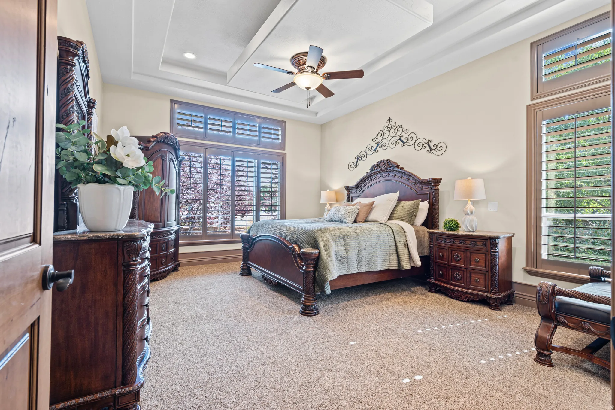 Carpeted room featuring a tray ceiling, ceiling fan, and plantation shutters