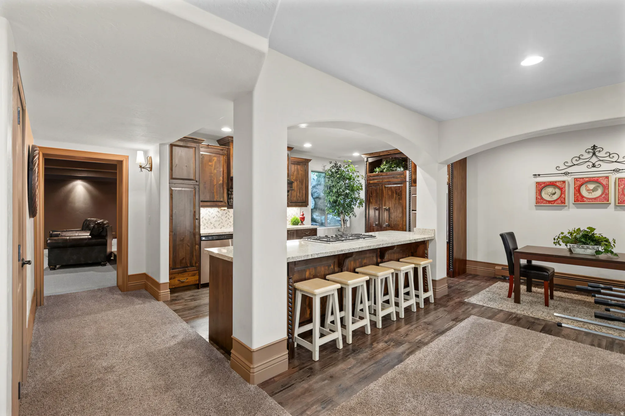 Open-concept kitchen featuring an eat-at island with a light-toned countertop, rich wood-finish cabinetry, and recessed lighting