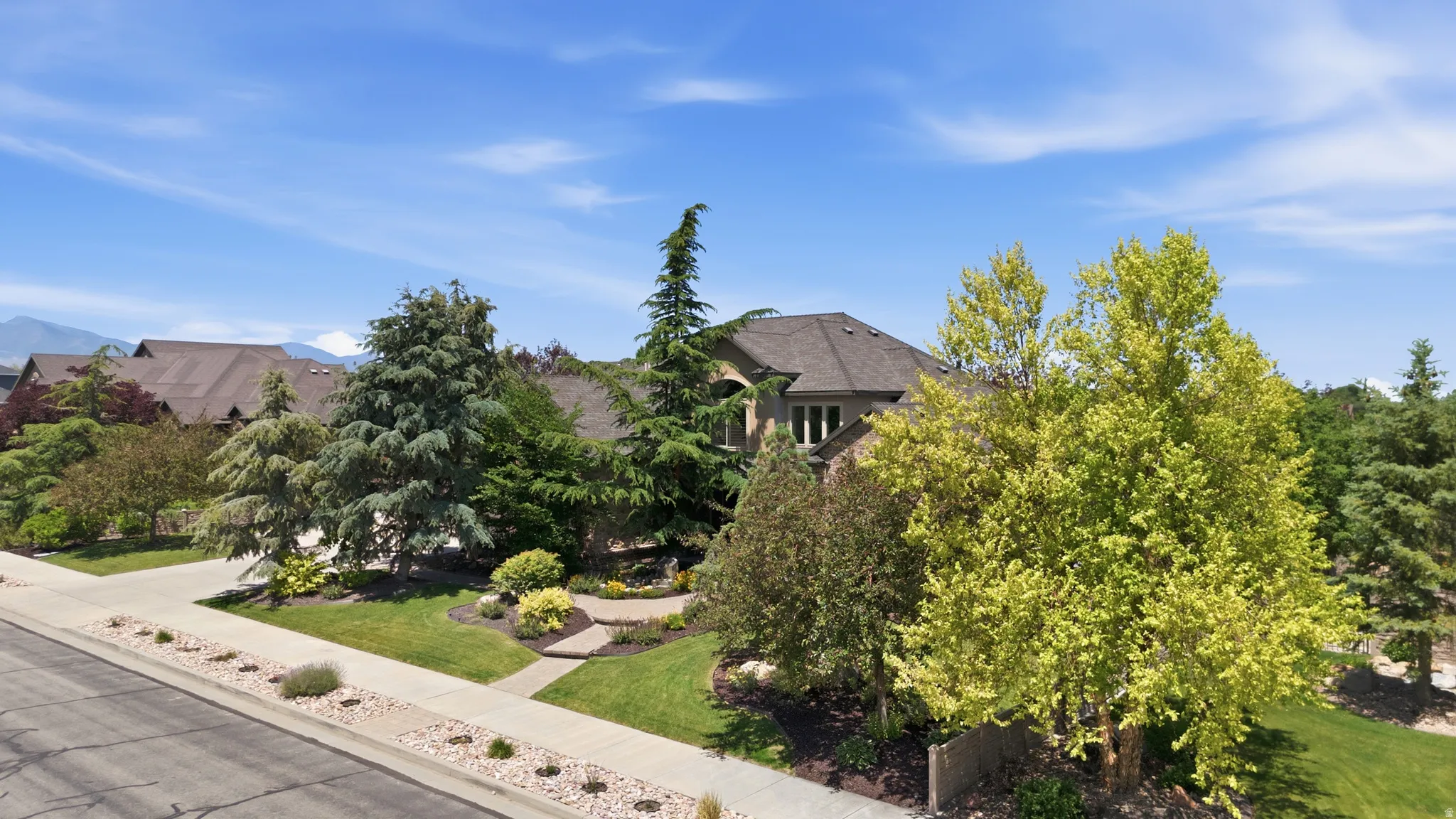Mature trees and landscaping frame this residence, featuring a pitched roofline and a stone facade