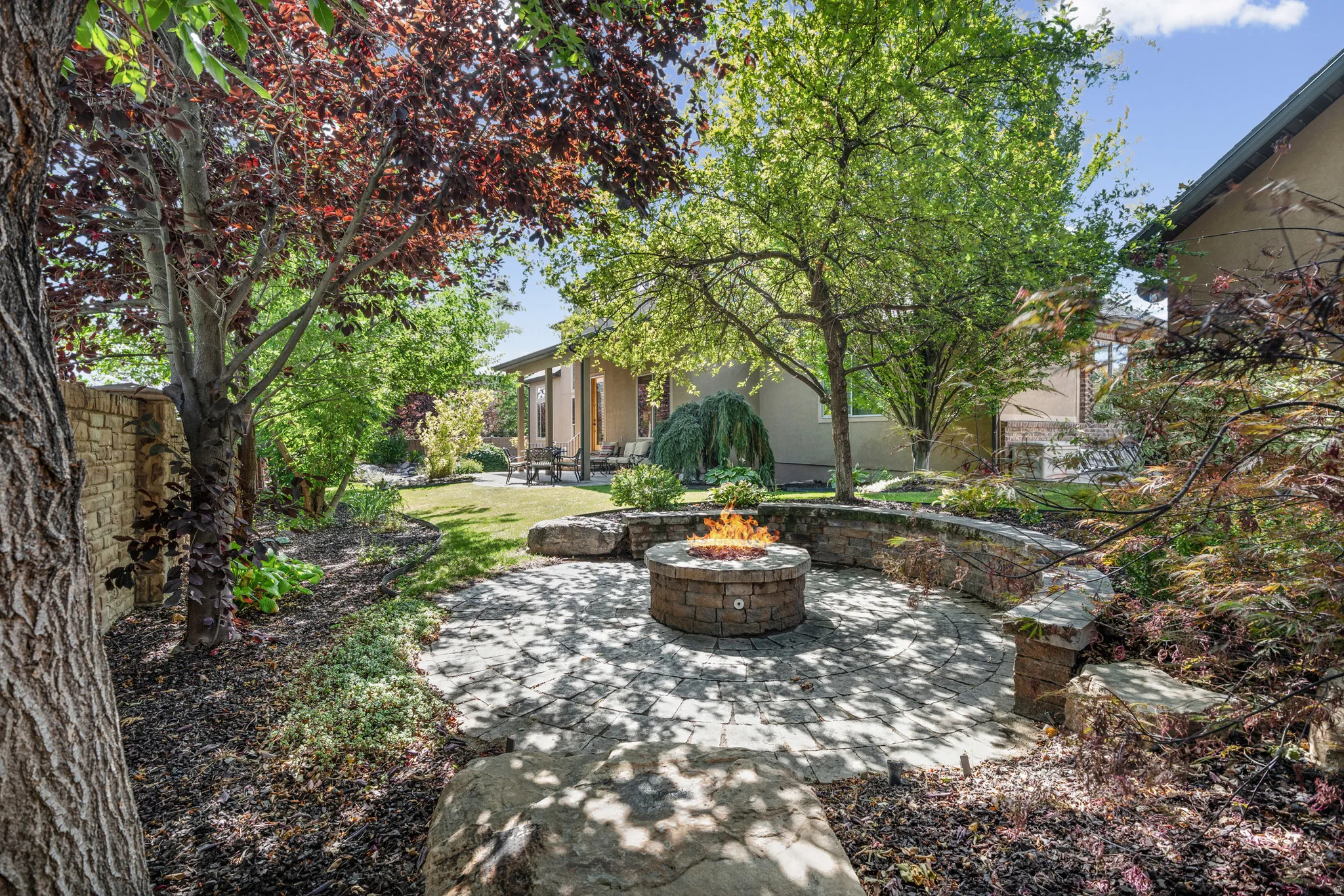 Stone-paved patio featuring a built-in fire pit with stone surround, complemented by a curved stone seating wall