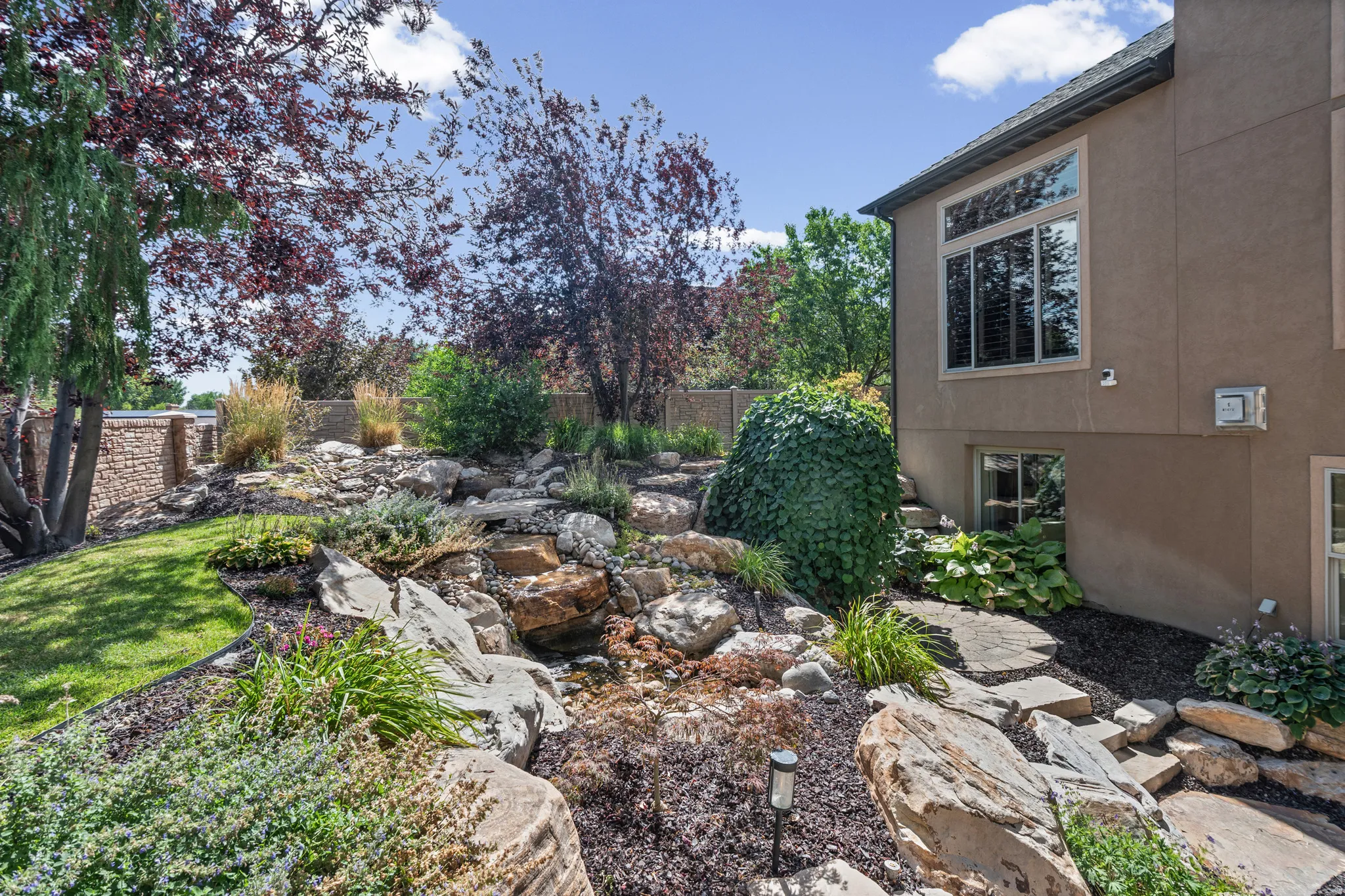 Exterior landscaping featuring natural rock formations, diverse plantings, and a stone retaining wall