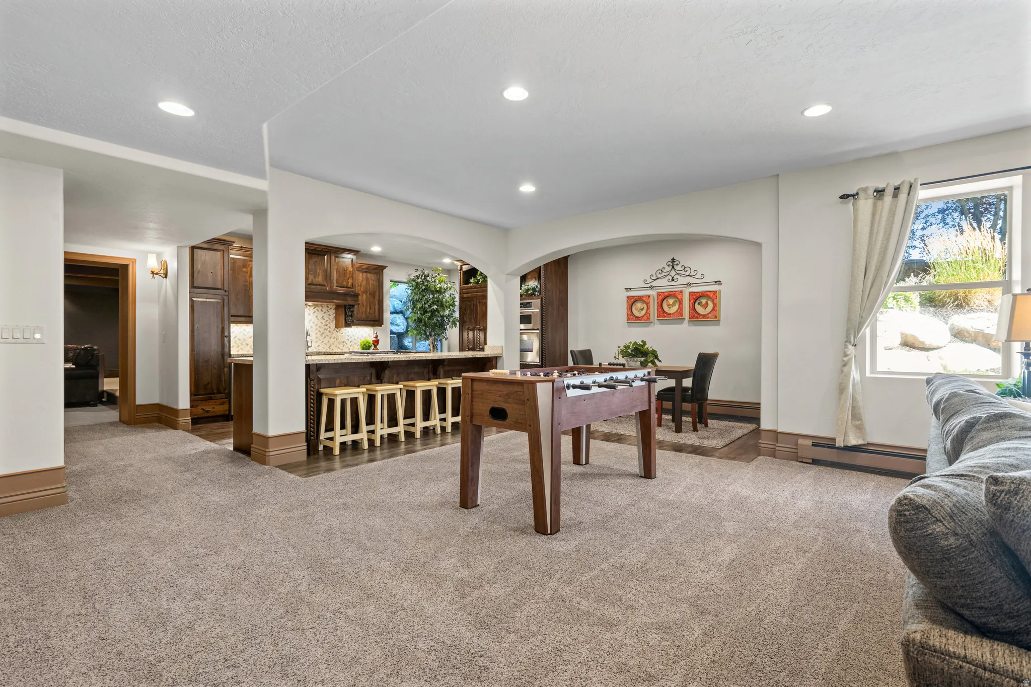 Expansive carpeted area featuring recessed lighting, a window with natural light, and a built-in wet bar with dark wood cabinetry