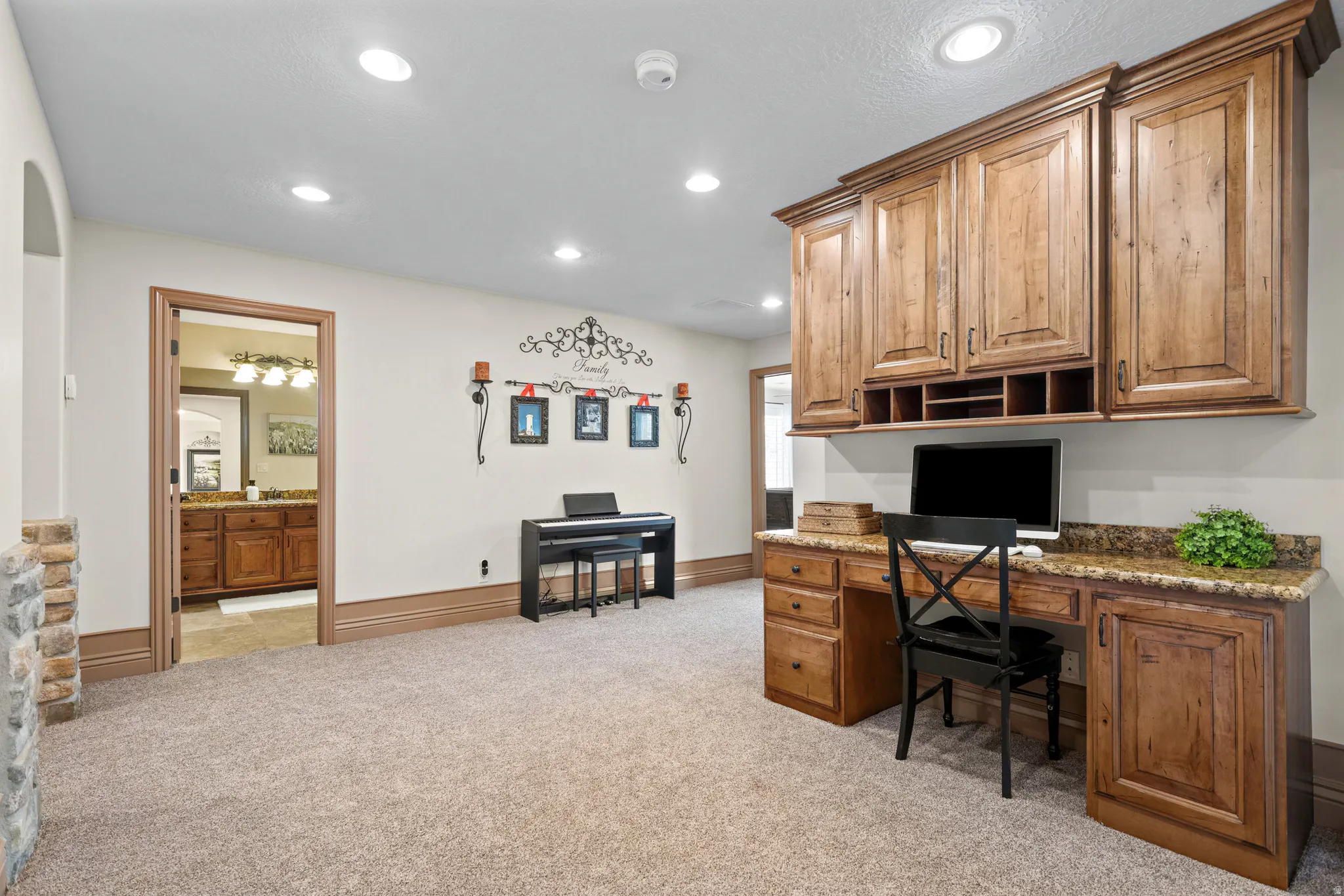 Built-in office cabinetry with a granite-style countertop, recessed lighting, carpet flooring, a stone-accented wall, and an arched entryway