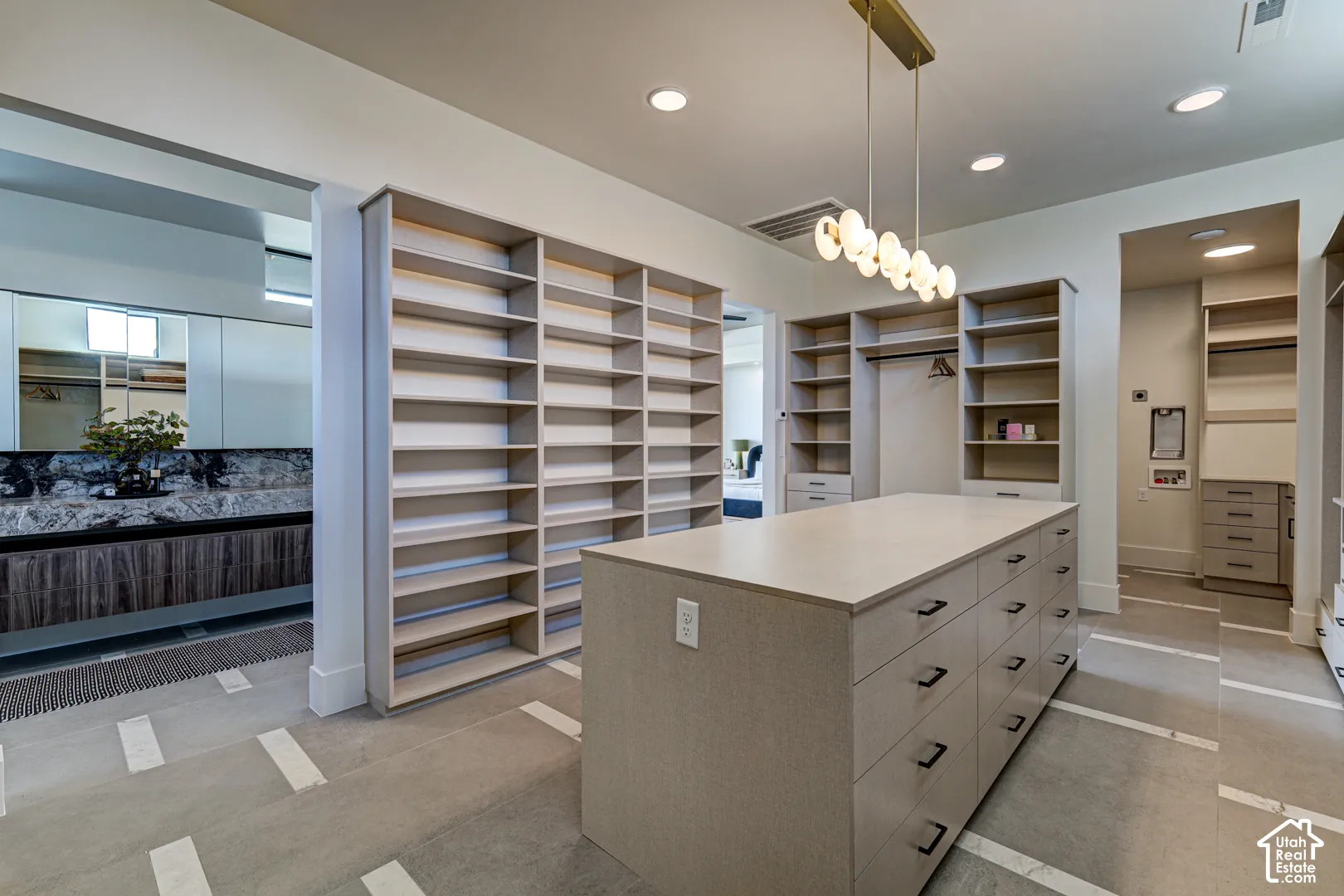 Custom built-in shelving, central storage island with drawers, modern linear chandelier, recessed lighting, and light-toned flooring