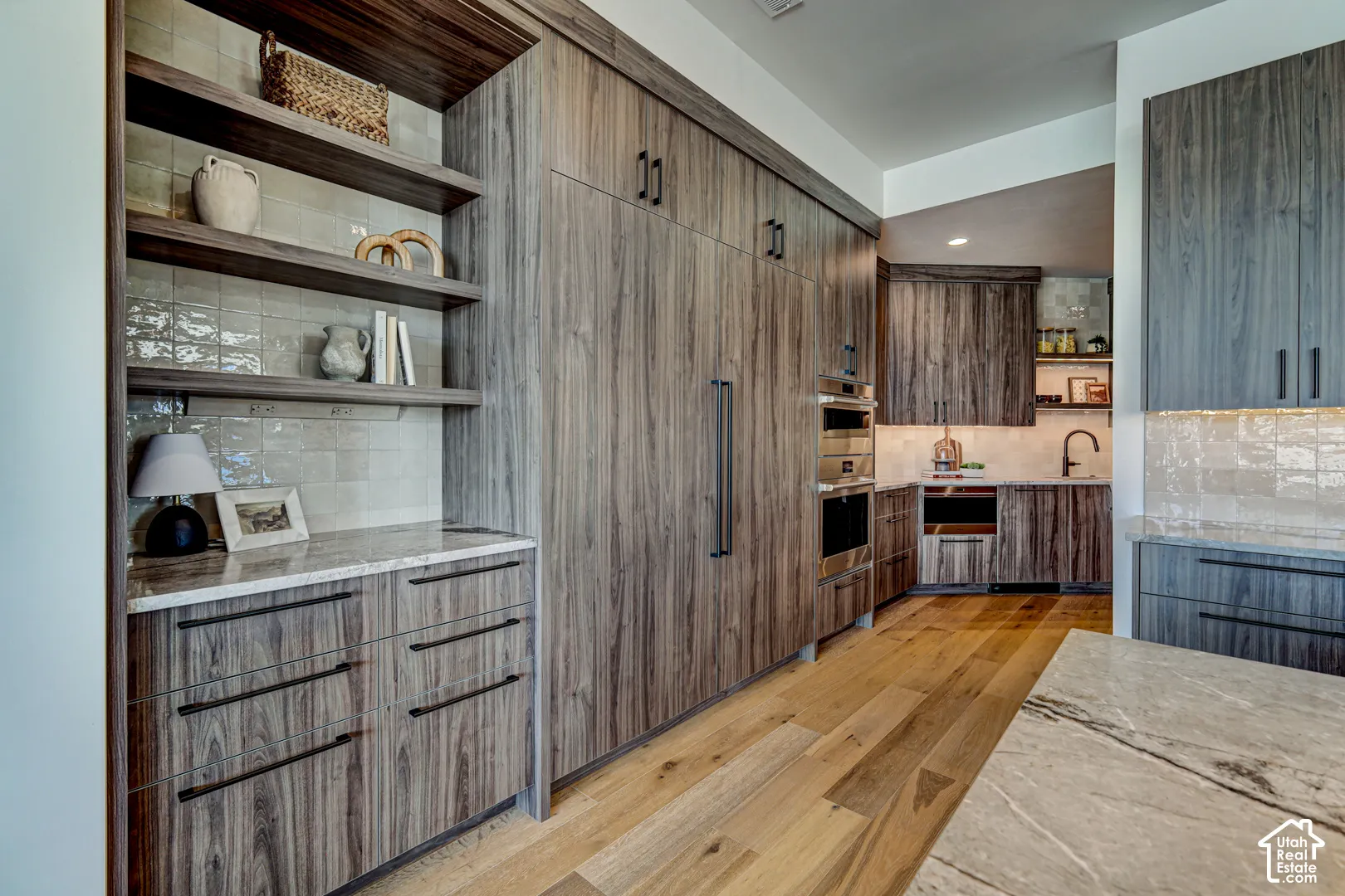 Full-height wood-finish cabinetry, integrated stainless steel appliances, wood-finish flooring, open shelving, and light-toned backsplash