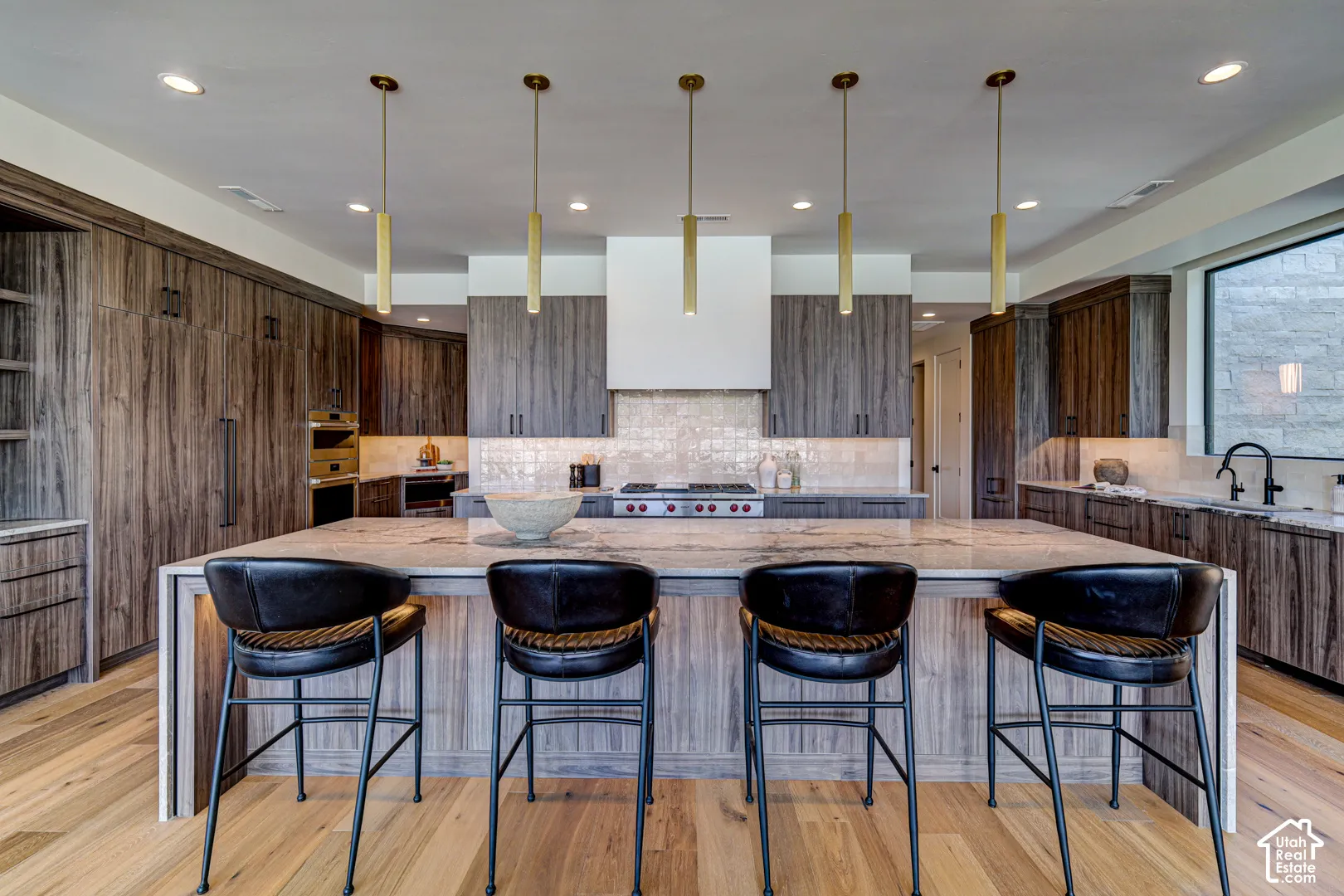 Spacious kitchen featuring a large island with countertop seating, wood-finish cabinetry, stainless steel appliances, and a tile backsplash