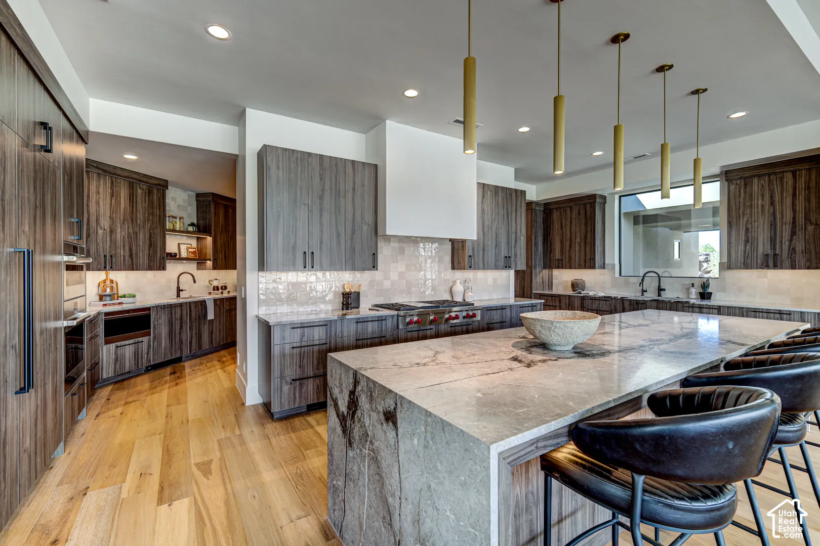 Gourmet kitchen featuring wood-finish cabinetry, a large center island with a waterfall edge, recessed lighting, and a built-in range with a modern hood