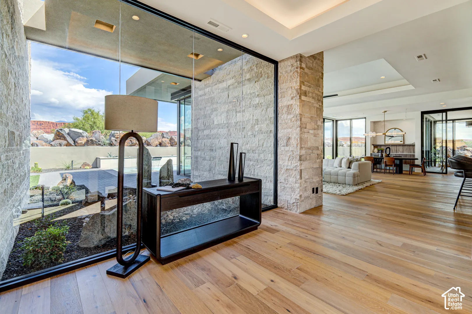 Hardwood flooring, stone accent wall, recessed lighting, expansive glass panels, and a tray ceiling