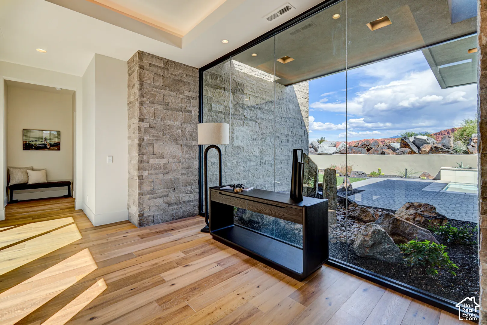 Hardwood-finish flooring, stone accent wall, recessed lighting, floor-to-ceiling glass panel, and rock landscaping