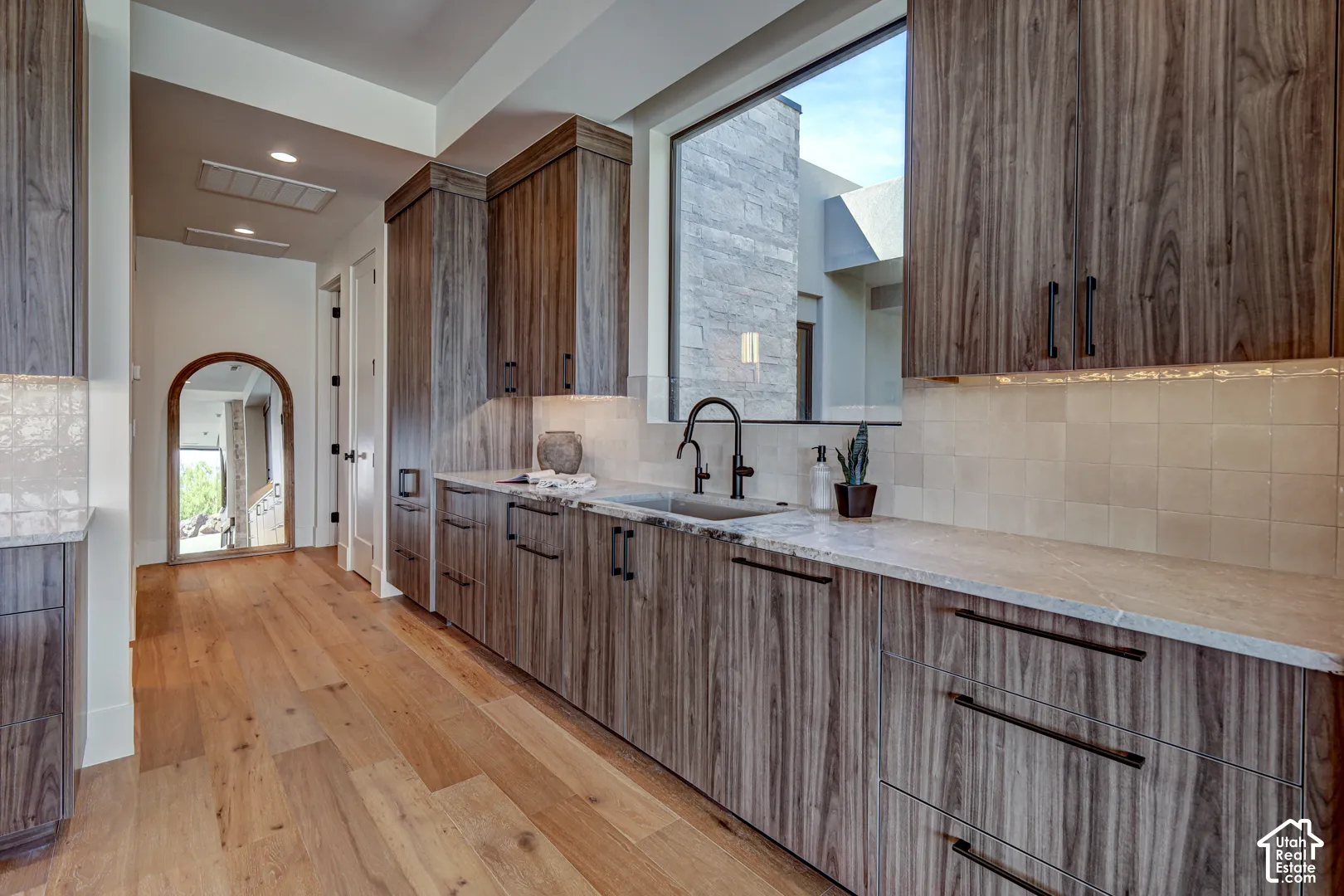 Wood-finish cabinetry, light-toned wood flooring, light-toned countertop, and a black-finish sink faucet
