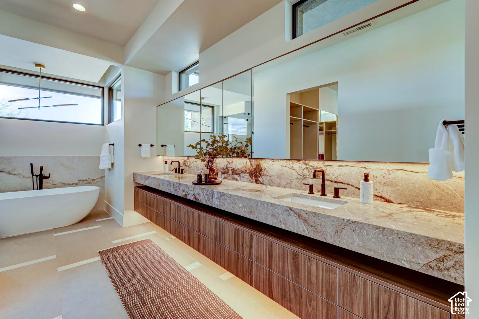 Floating double vanity with integrated sinks and stone countertop, freestanding bathtub with wall-mounted faucet, large wall mirror, and modern light fixtures