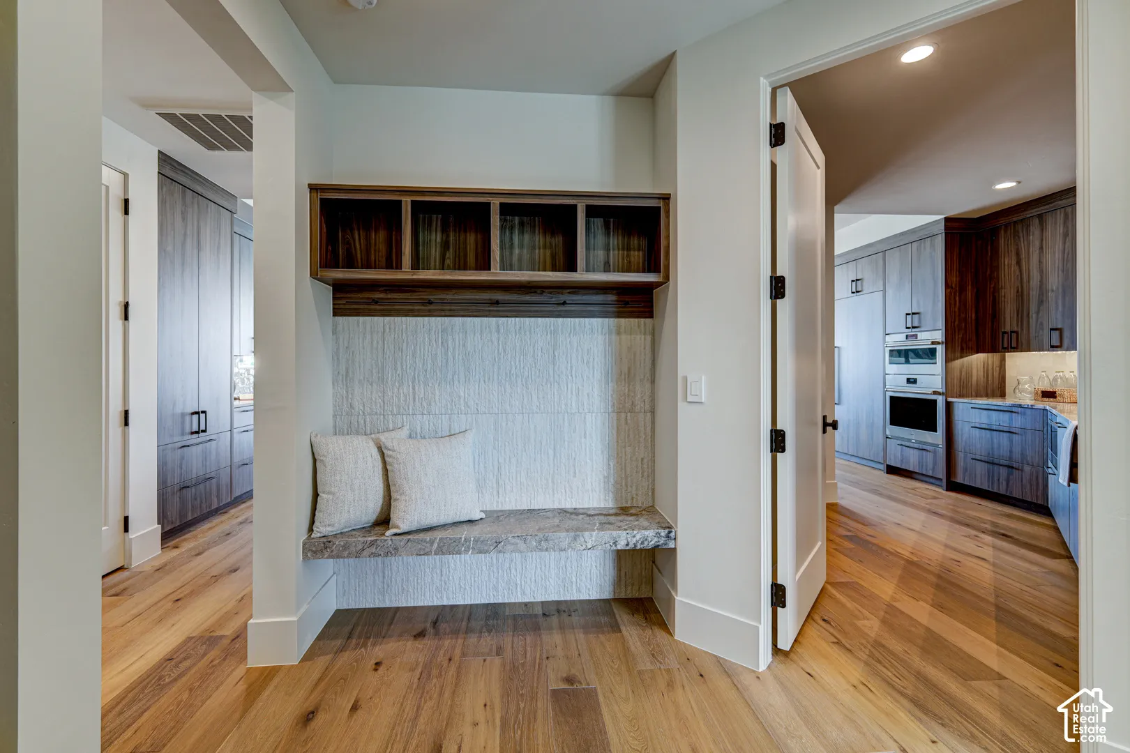 Hardwood flooring throughout, built-in mudroom bench with stone top, integrated wall cubbies, and a textured wall panel