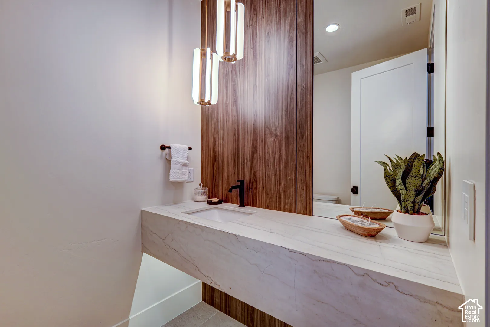 Floating vanity with integrated basin, stone-finish countertop, dark wood-finish accent wall, and contemporary pendant lighting