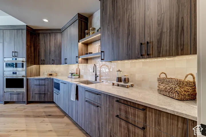 Custom cabinetry with wood-finish doors, integrated stainless steel appliances, light-toned backsplash tiling, and a built-in sink with a gooseneck faucet