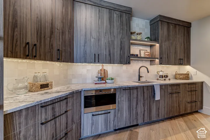 Wood-finish cabinetry with black hardware, under-cabinet lighting, light-toned backsplash, light-toned countertop, and a built-in microwave