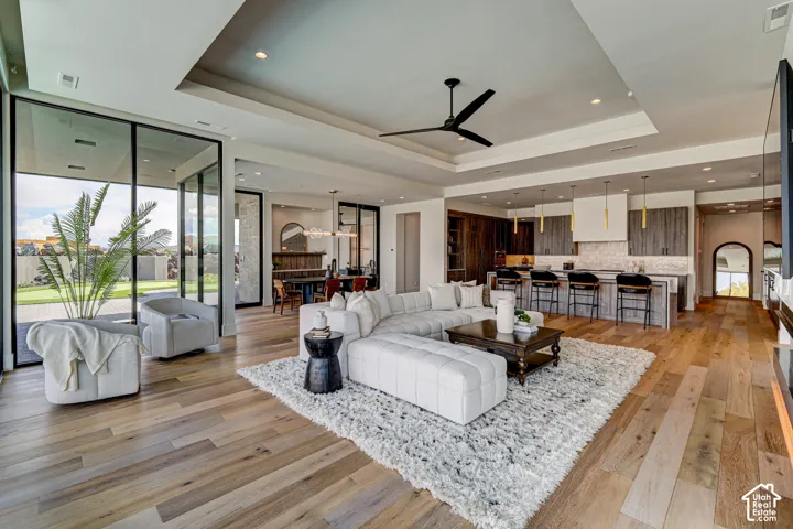 Expansive wood-finish flooring throughout, tray ceiling with recessed lighting and ceiling fan, full-height glass patio doors, and a kitchen featuring a large island with bar seating and pendant lighting