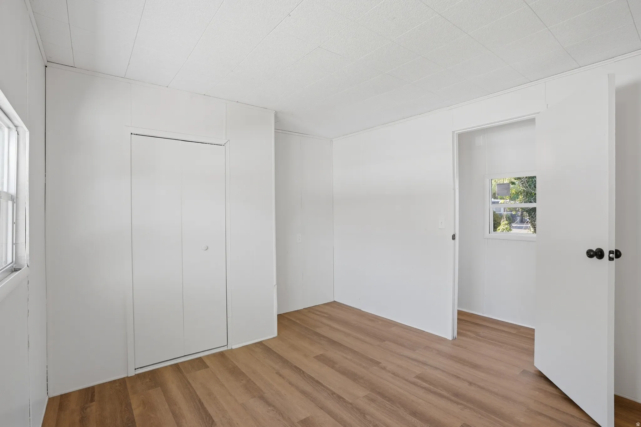 Bright room featuring wood-finish flooring, light paneled walls, and a white grid-patterned ceiling