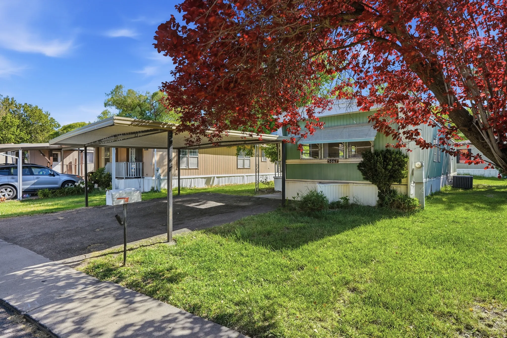 Property exterior with a green and white facade, featuring a paved driveway and an attached carport