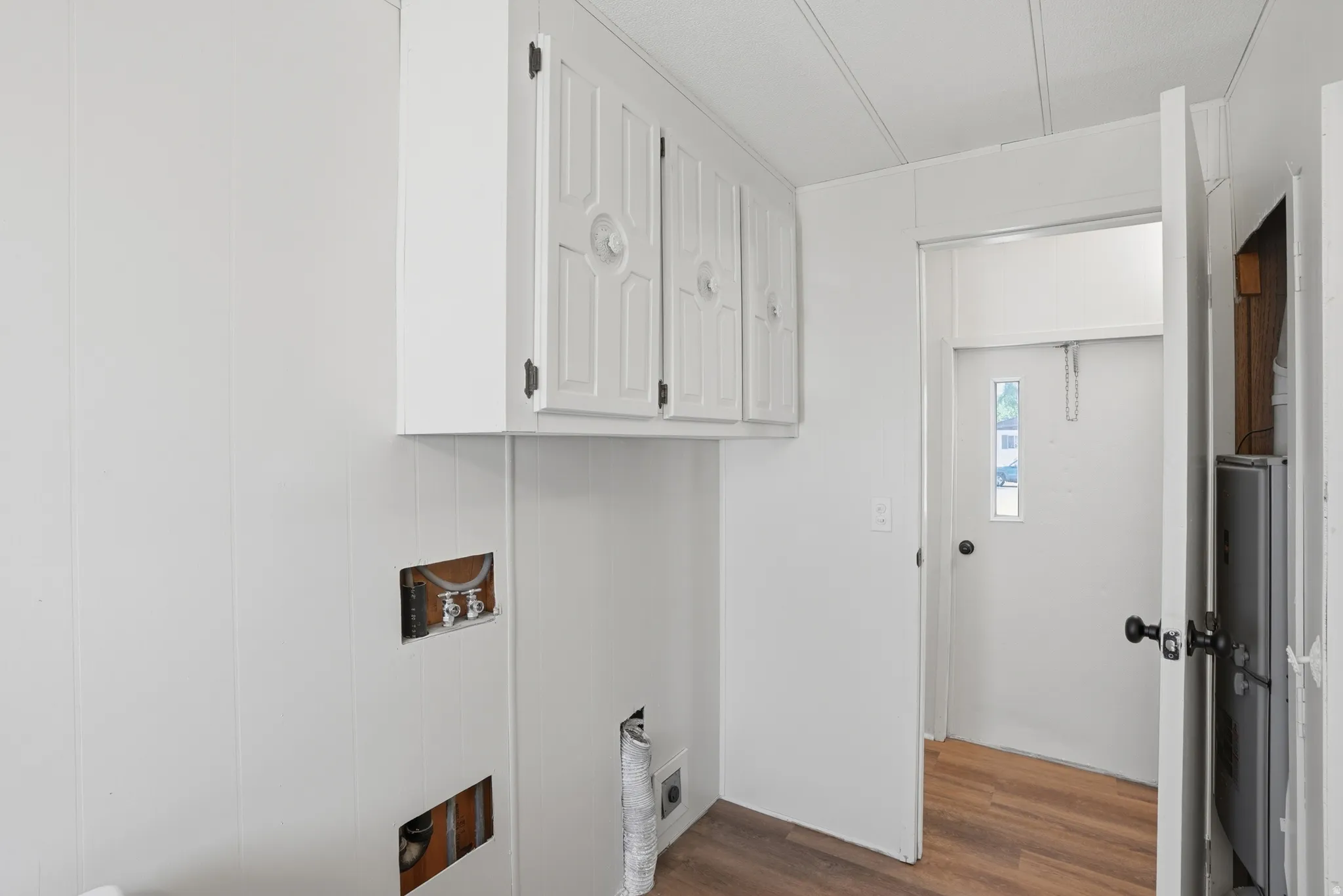 Utility area featuring light paneled walls, white upper cabinetry with dark hardware, and wood-finish flooring