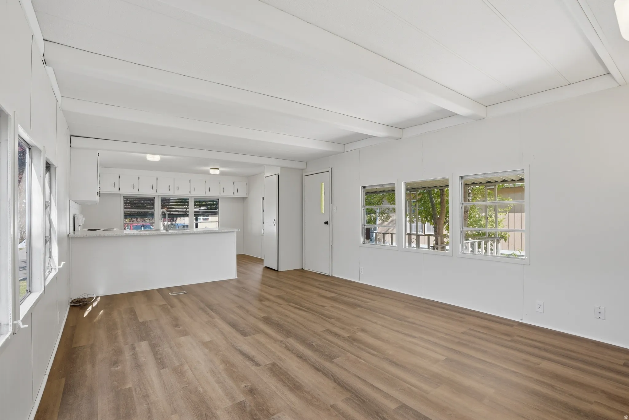 Open concept living space featuring wood-finish flooring, light walls, exposed ceiling beams, and multiple windows