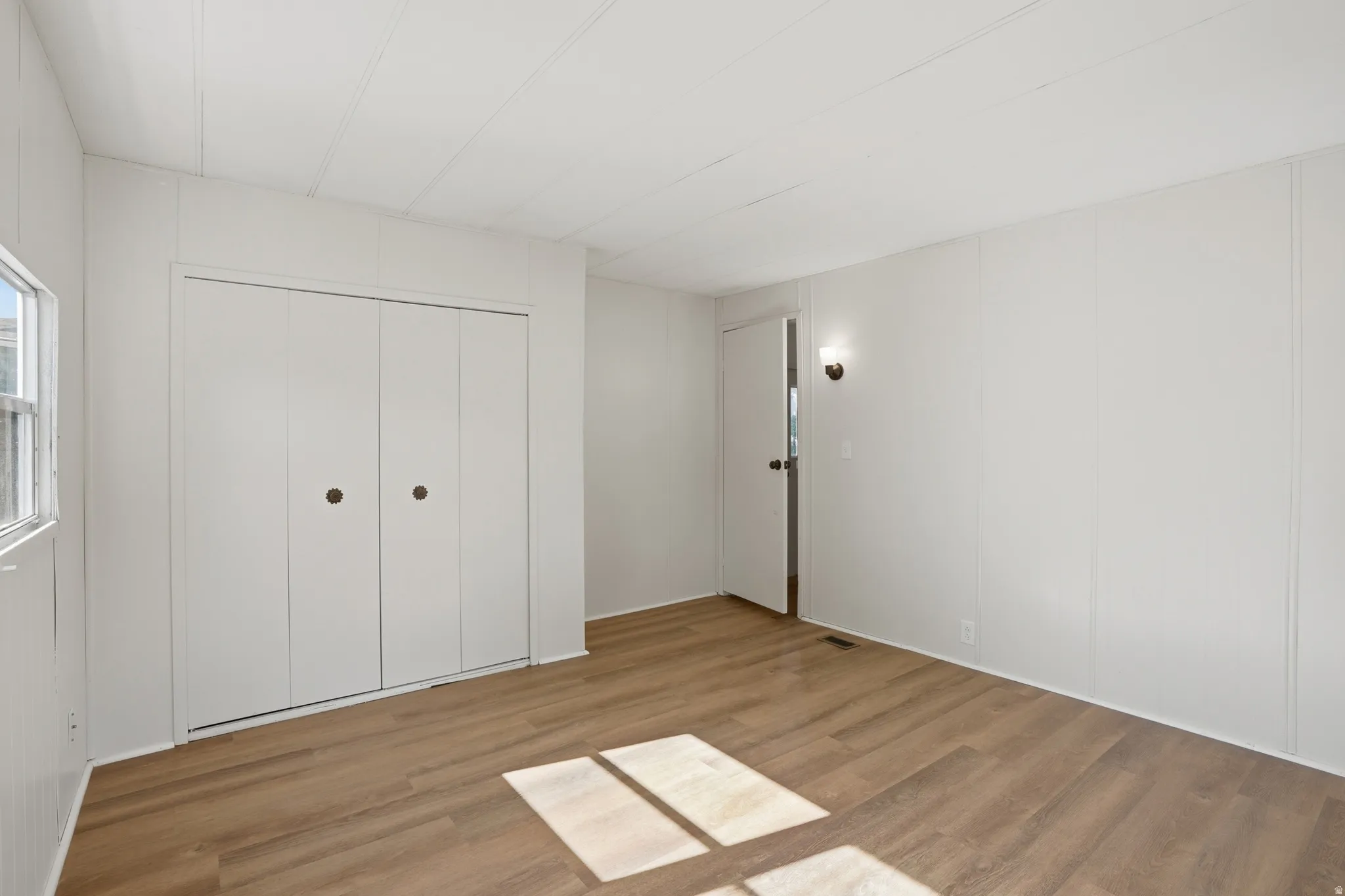 Room featuring wood-finish flooring, white paneling, and a bi-fold closet