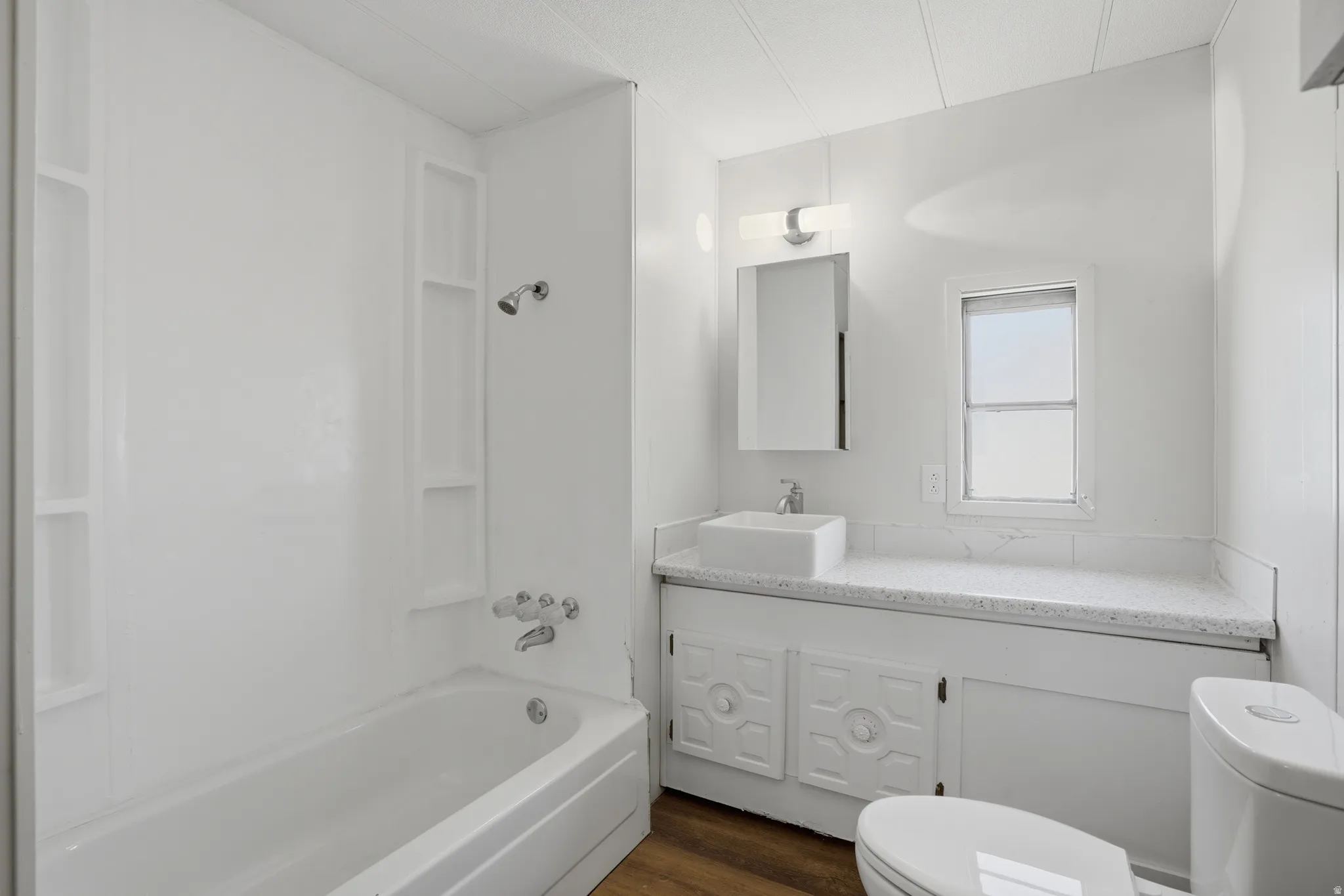 Bathroom featuring a white bathtub with integrated shelving, a rectangular vessel sink, and a vanity with a light-colored countertop