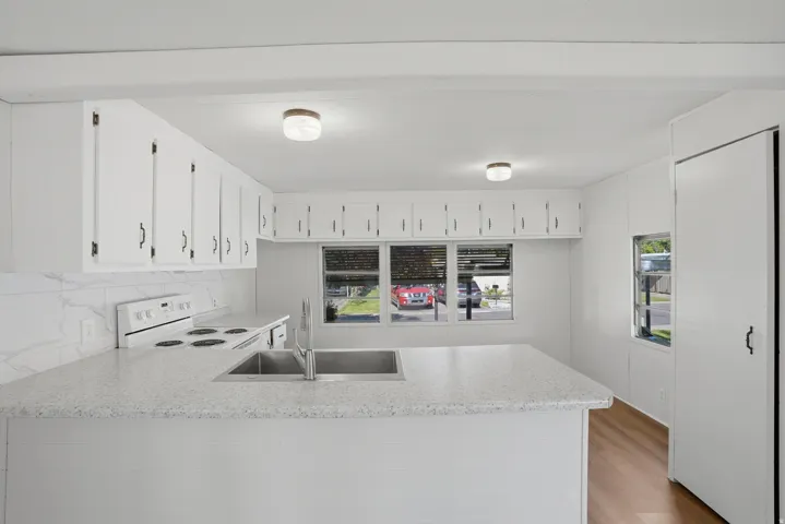 Bright kitchen featuring white cabinetry, a large basin stainless steel sink, wood-finish flooring, a white electric range, and a white tile backsplash