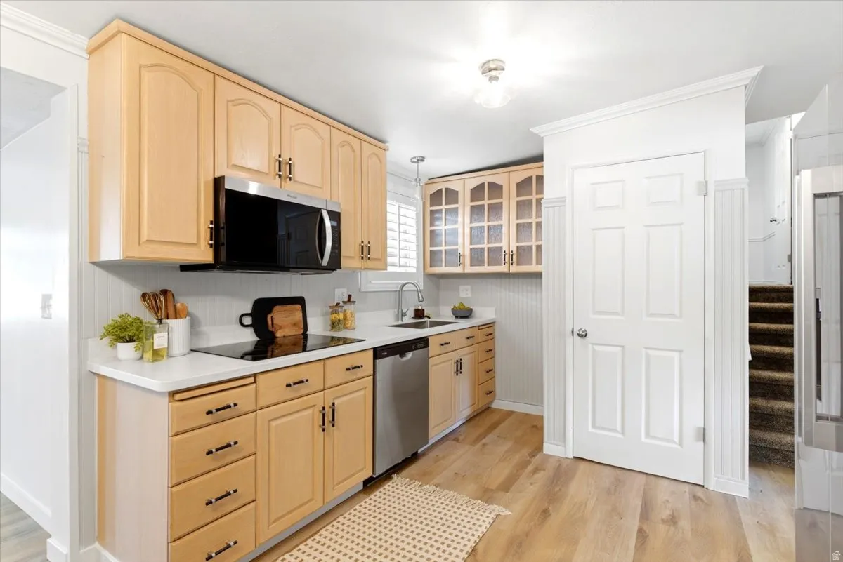 Kitchen featuring light wood-finish cabinetry with black hardware, white quartz countertops, stainless steel appliances, and wood-finish flooring
