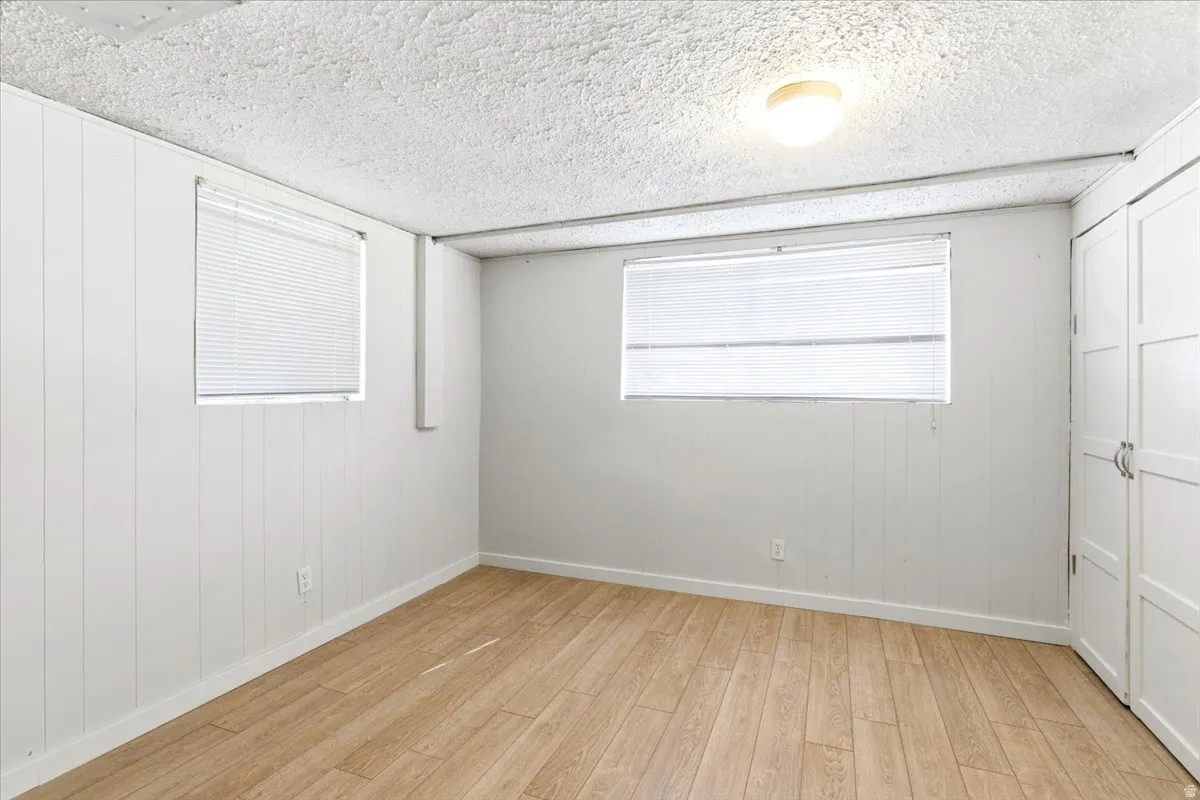 Room featuring light wood-finish flooring, white vertical plank wall panels, two windows with blinds, a ceiling-mounted light fixture, and built-in closet storage with panel doors