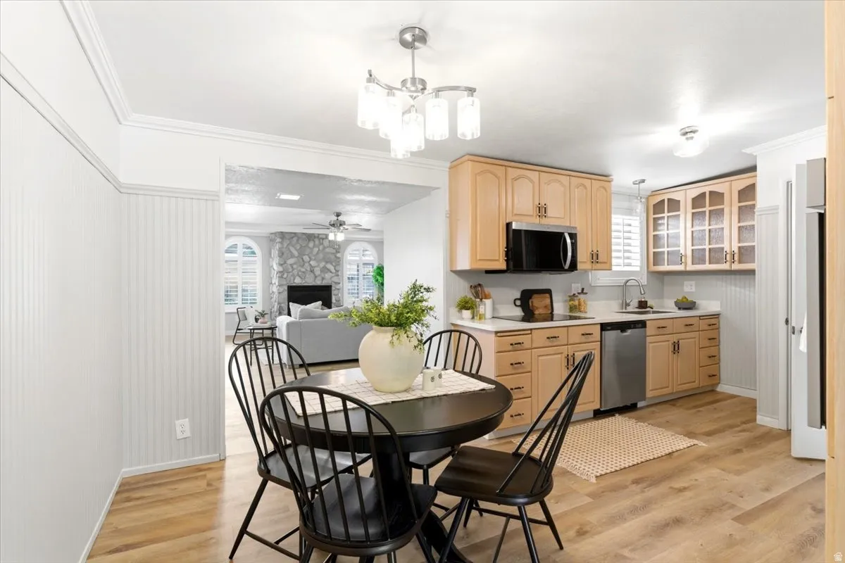 Open-concept kitchen and dining area featuring natural wood cabinetry, stainless steel appliances, wood-finish flooring, and crown molding