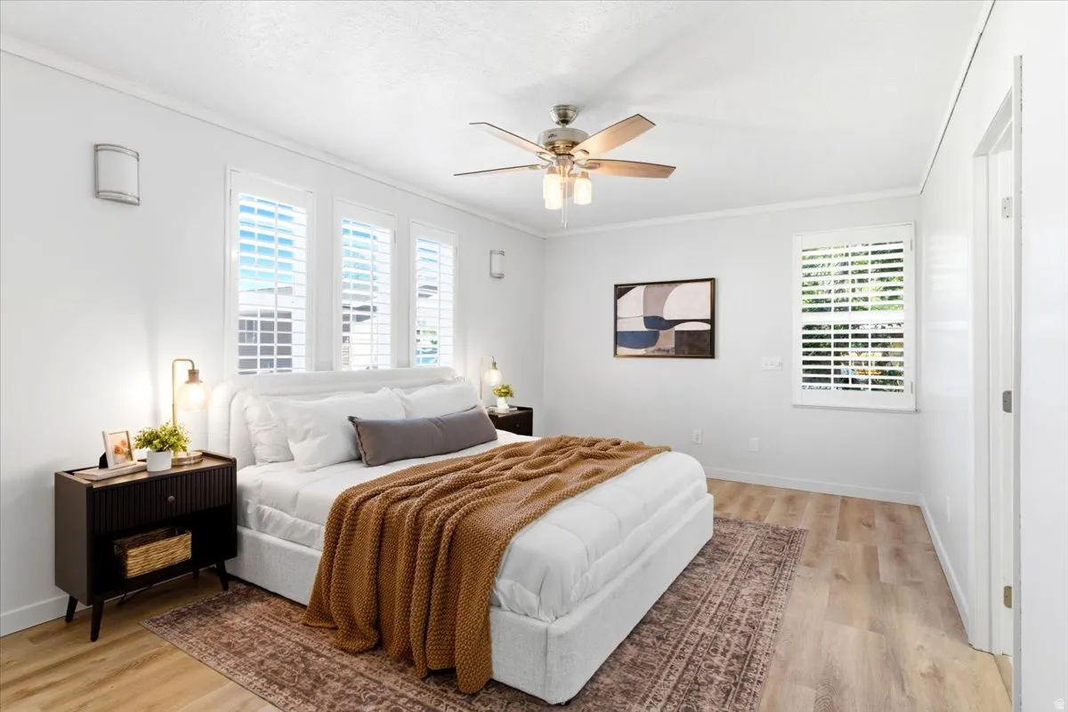 Bedroom featuring three windows with plantation shutters, wood-finish flooring, and a ceiling fan with integrated lighting