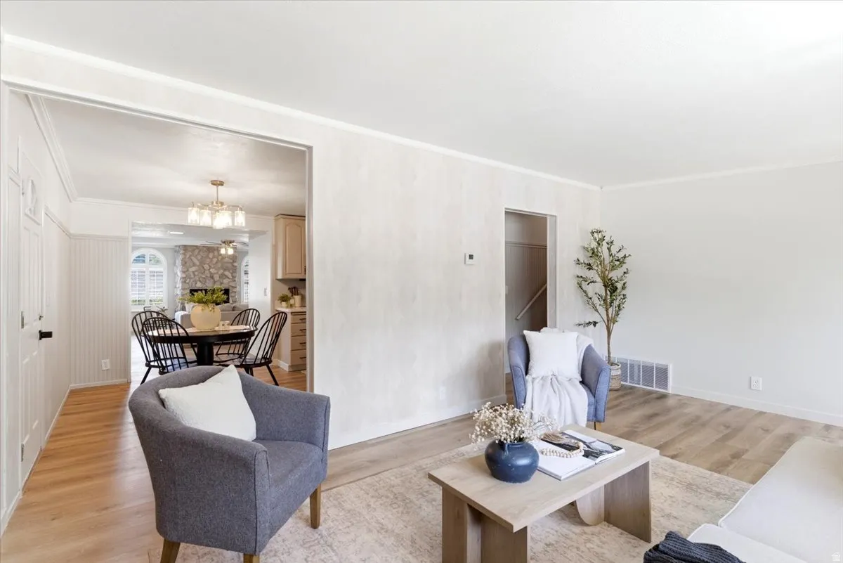 Light wood-finish flooring throughout, crown molding, and a wide entryway leading to a dining area with a stone-clad fireplace and arched window