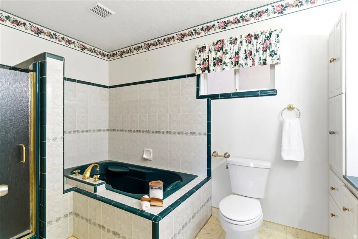 Bathroom featuring a built-in tub, tiled shower with frosted glass, and a toilet