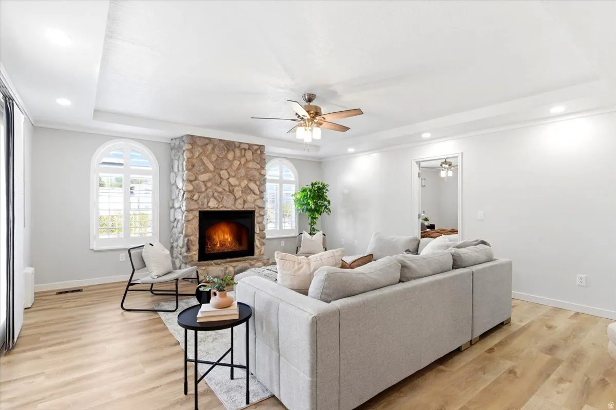 Living area featuring a stone fireplace, arched windows, tray ceiling, recessed lighting, and wood-finish flooring
