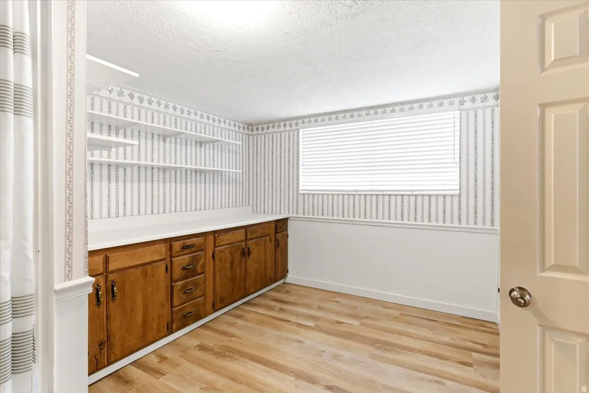 Room featuring wood-finish flooring, a window with horizontal blinds, built-in lower cabinetry with a continuous countertop, and wall-mounted shelving
