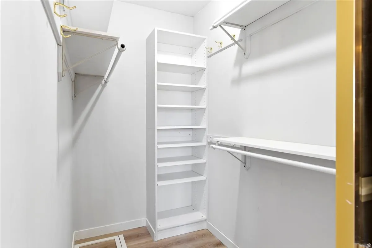 Walk-in closet featuring built-in shelving, two hanging rods, two upper shelves, and wood-finish flooring