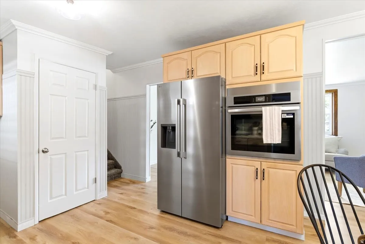 Kitchen featuring wood-finish flooring, light wood cabinetry, stainless steel refrigerator, and a built-in stainless steel oven