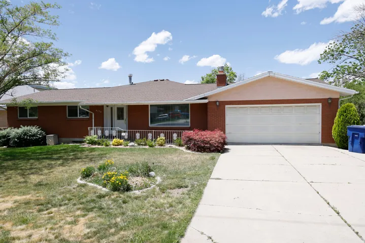Brick exterior home featuring an attached garage, paved driveway, and established front landscaping