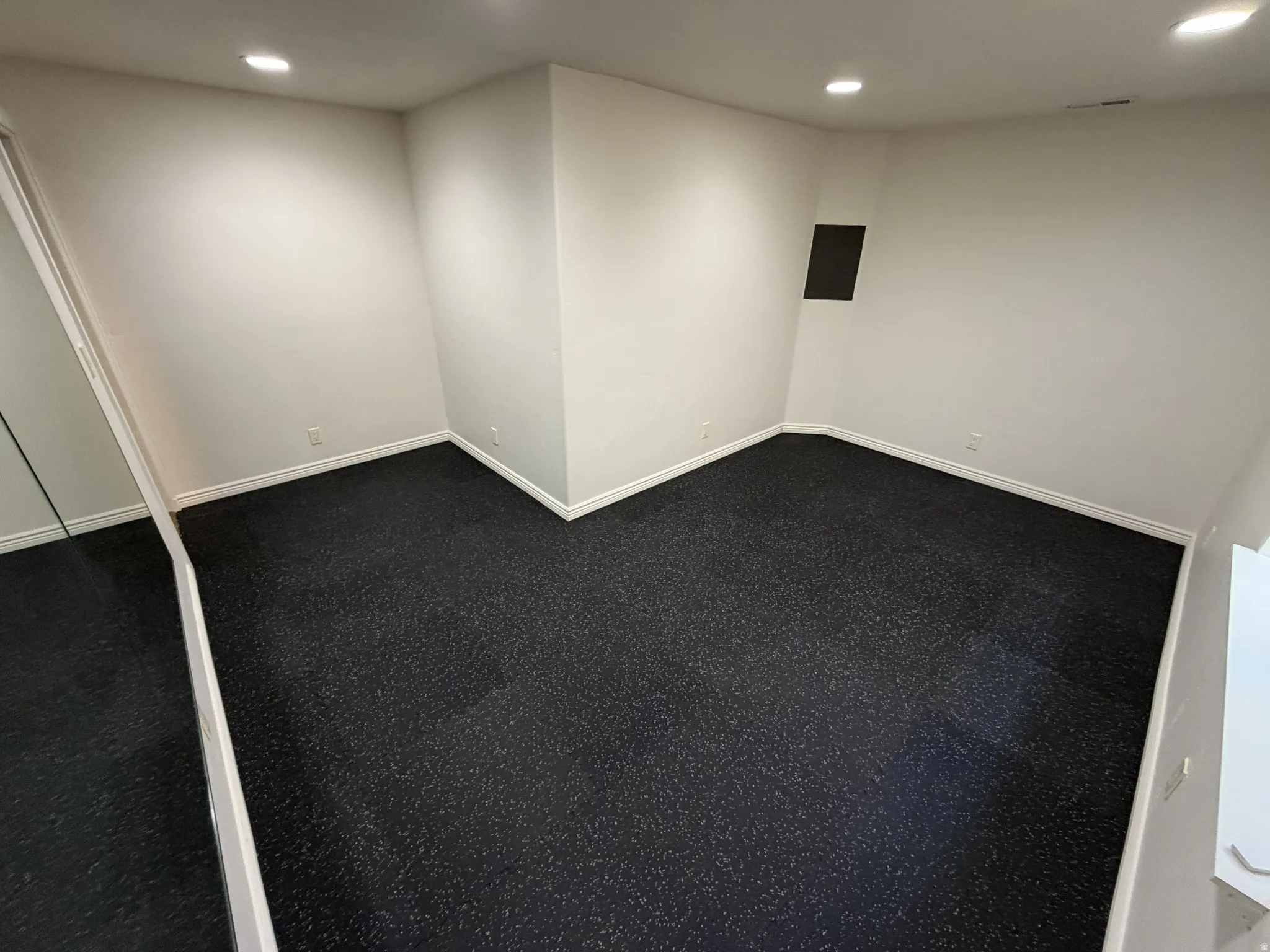 Spacious room with dark speckled flooring, white baseboards, and recessed lighting