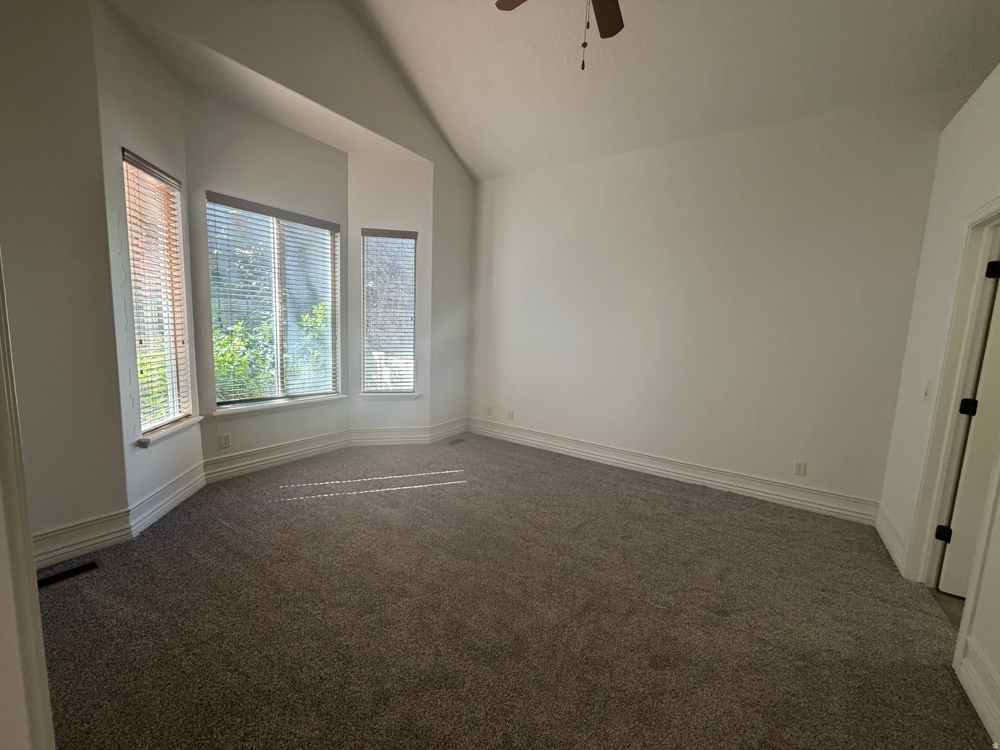 Spacious room featuring a bay window with three individual windows, vaulted ceiling, neutral wall paint, and gray carpet flooring