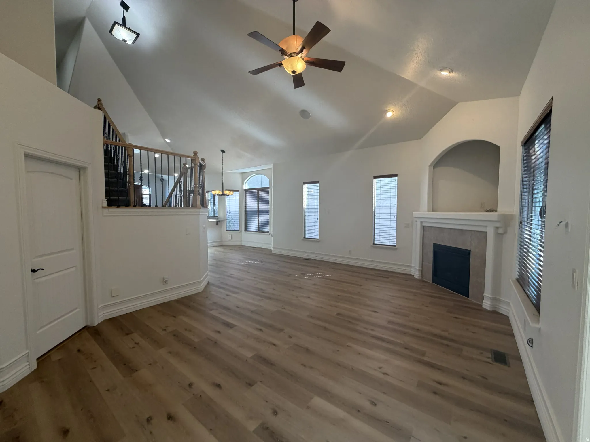 Spacious living area featuring vaulted ceilings, wood-finish flooring, and a fireplace with a tiled surround