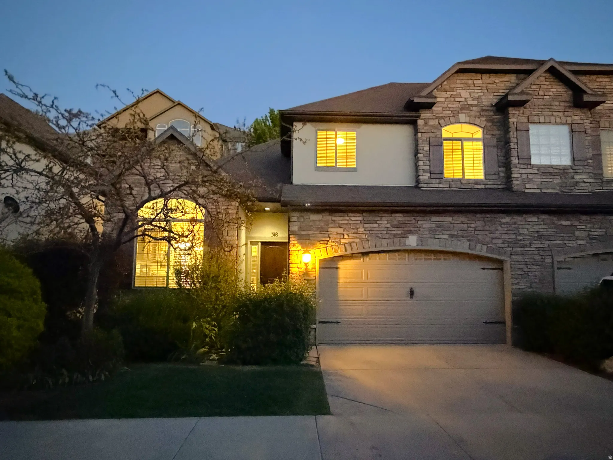 Stone and stucco exterior featuring an arched entryway, integrated garage with arched stone surround, decorative window shutters, and a well-maintained front yard with mature landscaping