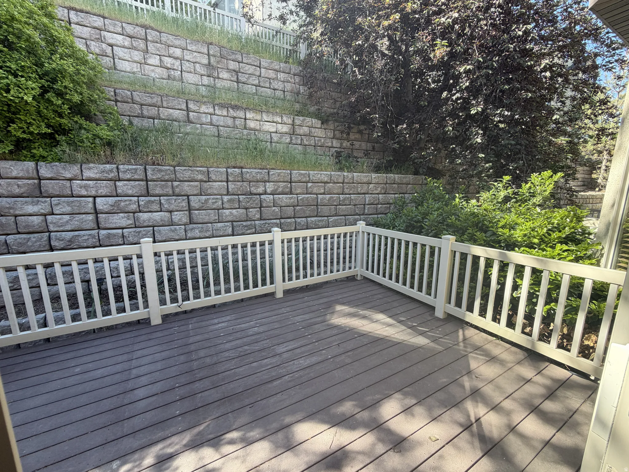 Spacious outdoor deck featuring composite decking, white picket railing, and a tiered stone retaining wall