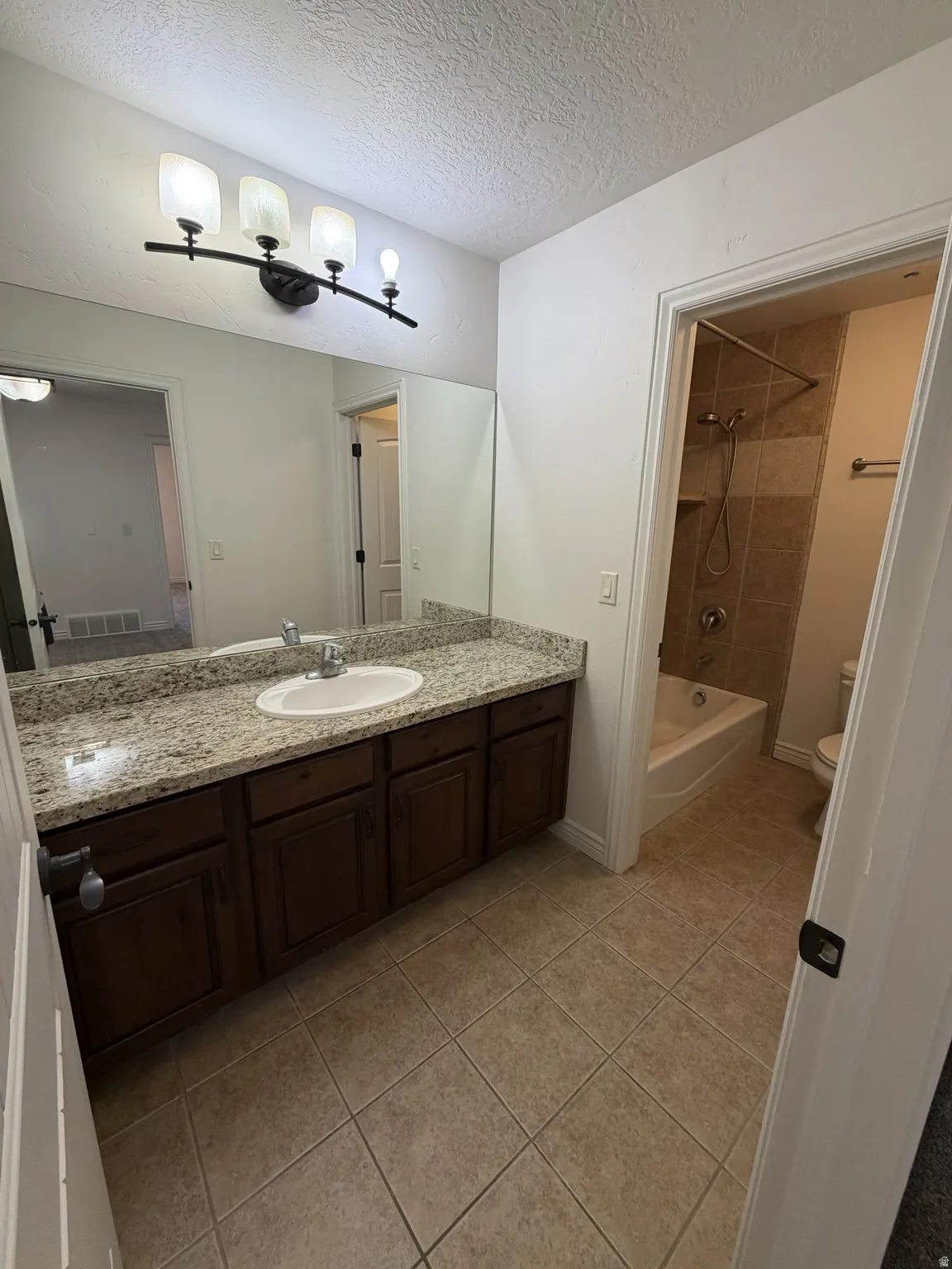 Bathroom featuring a dark wood-finish vanity with a light speckled countertop, an integrated sink, and a large wall mirror